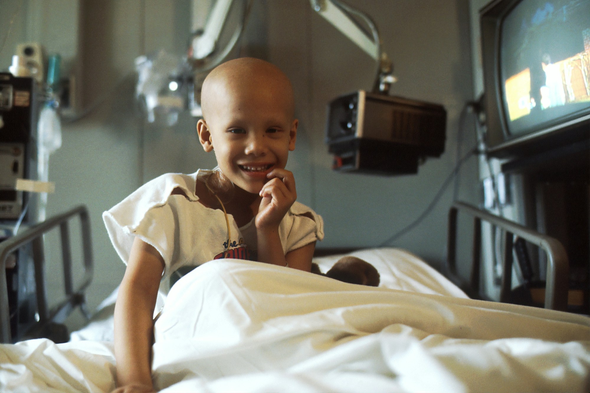 A young patient smiling from a hospital bed during treatment