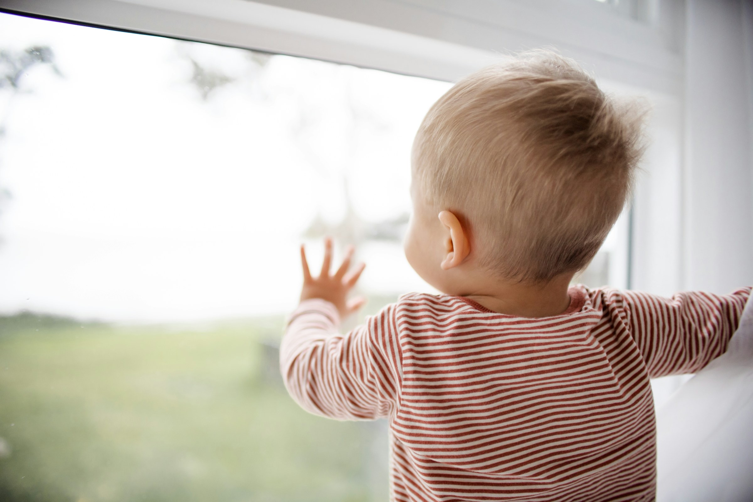 A toddler at a window, reaching towards the light